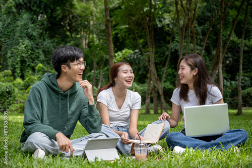 A group of cheerful Asian students in casual clothes sits and talks in the green park, enjoying their conversation while working on their co-project together.