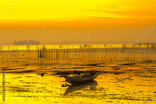 A small wooden boat rests on the calm water of a beach in Bangkalan, Madura, Indonesia at sunset. photo