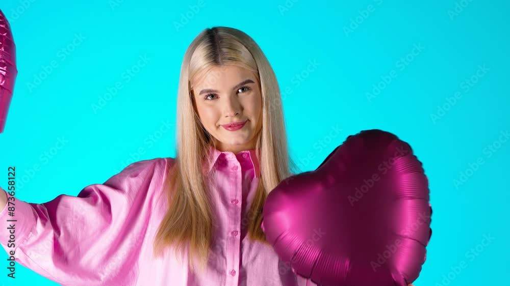 Pretty Blonde Woman Holding Waving Purple Heart Balloons While Looking At Camera, Colorful Studio Shot Pretty Blonde Woman Holding Waving Purple Heart Balloons While Looking At Camera, Colorful Studio Shot