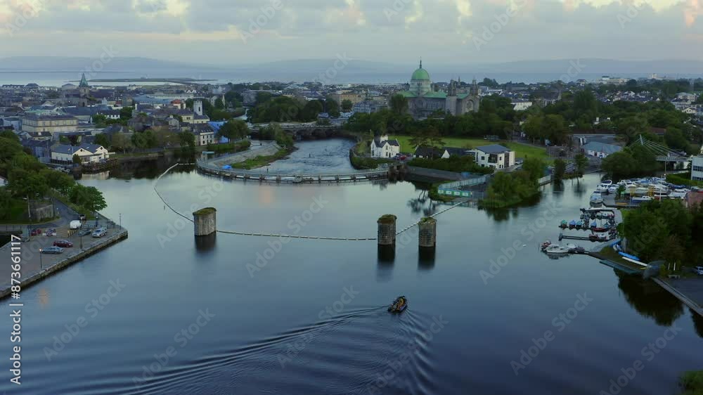 Aerial orbit around small boat near Salmon Weir with Galway cathedral behind at sunset Aerial orbit around small boat near Salmon Weir with Galway cathedral behind at sunset
