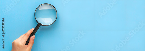 Biology business working dedective searching concept banner - Close up of a magnifying glass, isolated on blue table background, top view