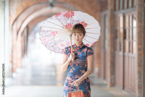 Young Taiwanese woman in her 20s wearing a blue cheongsam, strolling through a cultural district in Wanhua, Taipei, Taiwan, while holding a Chinese-patterned umbrella photo