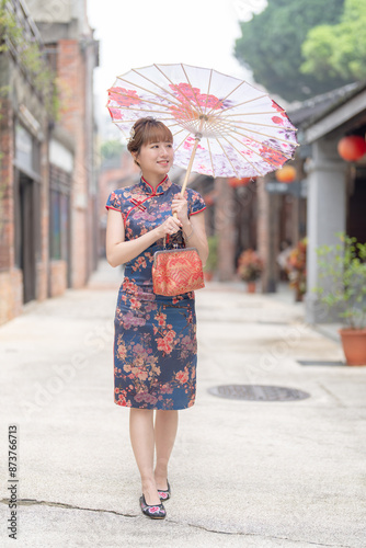 Young Taiwanese woman in her 20s wearing a blue cheongsam, strolling through a cultural district in Wanhua, Taipei, Taiwan, while holding a Chinese-patterned umbrella photo