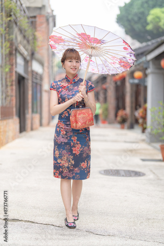 Young Taiwanese woman in her 20s wearing a blue cheongsam, strolling through a cultural district in Wanhua, Taipei, Taiwan, while holding a Chinese-patterned umbrella photo