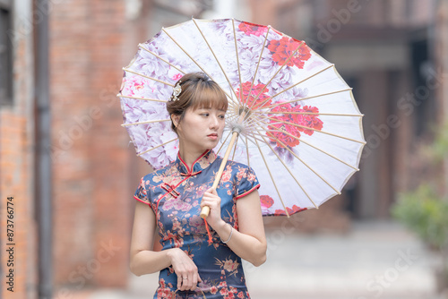 Young Taiwanese woman in her 20s wearing a blue cheongsam, strolling through a cultural district in Wanhua, Taipei, Taiwan, while holding a Chinese-patterned umbrella photo