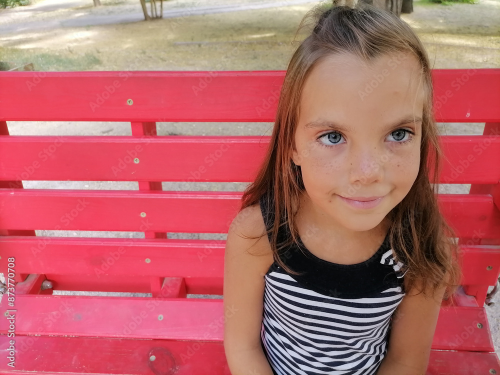 The girl sits on a bench in park. There is a flower ornament on her head The girl sits on a bench in park. There is a flower ornament on her head