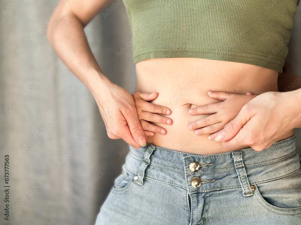 Close up of woman in jeans and green top with childs hands on her waist. Concept of family bonding, motherhood, and affection. Neutral background Close up of woman in jeans and green top with childs hands on her waist. Concept of family bonding, motherhood, and affection. Neutral background