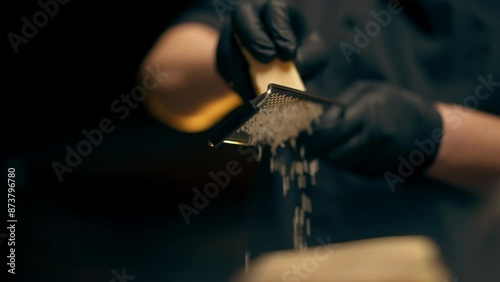 close up in a restaurant in a rib bar in the central hall with yellow lighting, a chef in black gloves grates a block of cheese on a plate with sliced meat