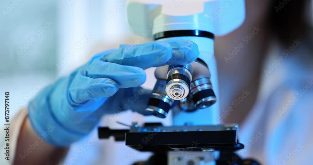 Laboratory worker in uniform turns microscope lenses Laboratory worker in uniform turns microscope lenses