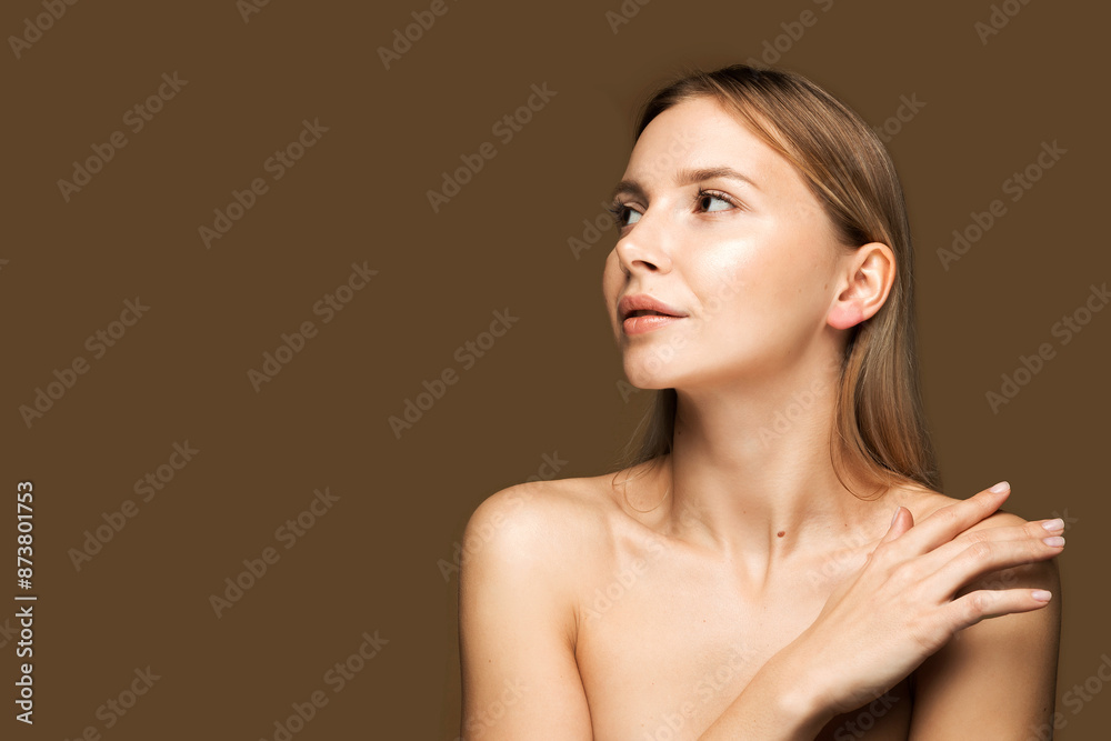 Young Woman on Brown Background with Space for Text. A young Caucasian woman with smooth, youthful skin. She looks away, touching her shoulder. Brown background with space for text. Young Woman on Brown Background with Space for Text. A young Caucasian woman with smooth, youthful skin. She looks away, touching her shoulder. Brown background with space for text.
