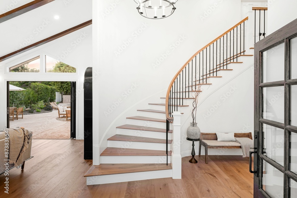 Fototapeta premium home interior with a curved staircase, wooden floors, and a view of the patio through open doors.