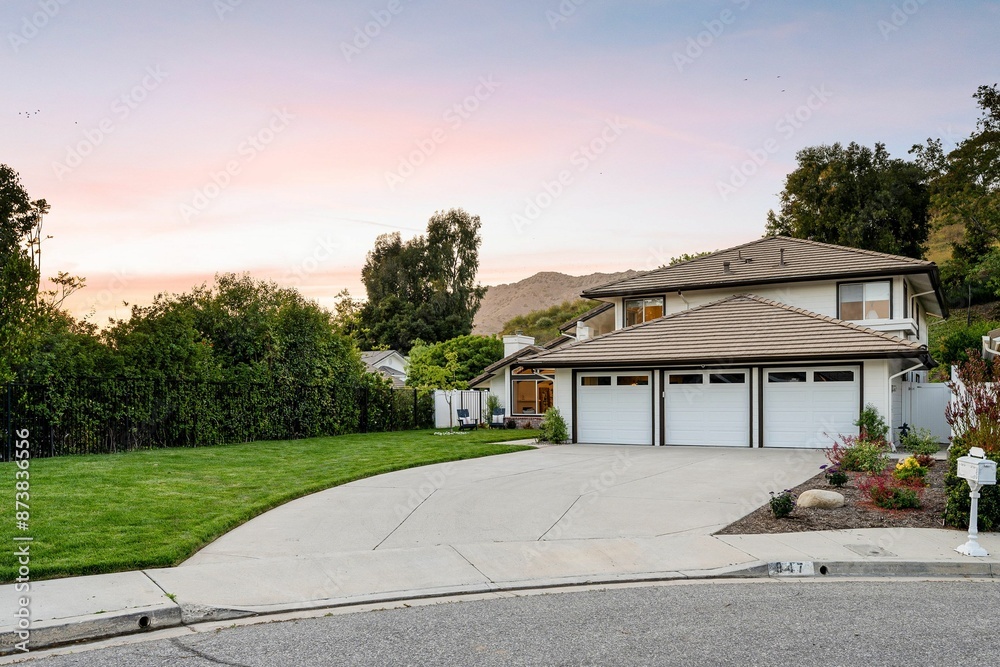 Fototapeta premium two-story house with a three-car garage, well-maintained lawn, and a scenic background at sunset