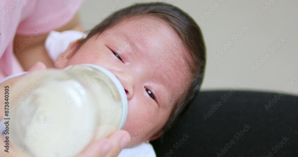 Sleepy newborn baby sucking out some milk from a baby bottle used to feed her as she is falling asleep in her mother's arms. Sleepy newborn baby sucking out some milk from a baby bottle used to feed her as she is falling asleep in her mother's arms.