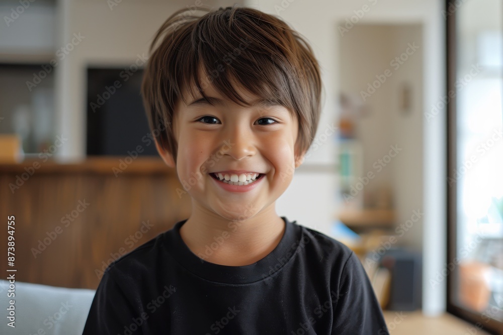 A young boy with short brown hair is smiling and looking at the camera. He is wearing a black shirt and sitting on a couch A young boy with short brown hair is smiling and looking at the camera. He is wearing a black shirt and sitting on a couch