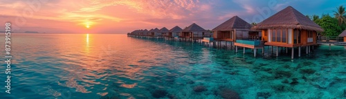 panoramic view of luxury overwater bungalows with glass floors over clear turquoise waters, sunset backdrop