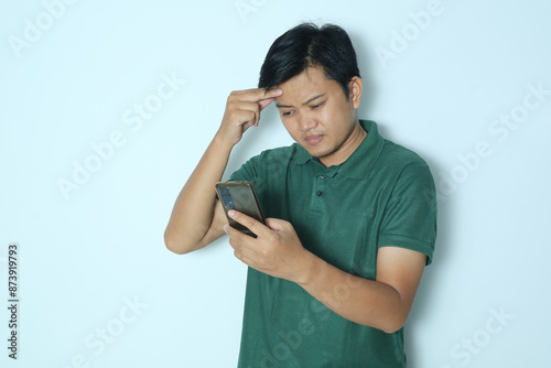 Asian man showing sad expression looking at smartphone. Wearing a green t-shirt photo