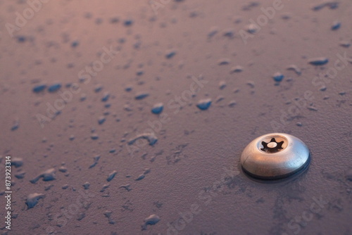 Macro of shiny metal bolt screwed in a plastic dark blue board with raindrops on it, well lit