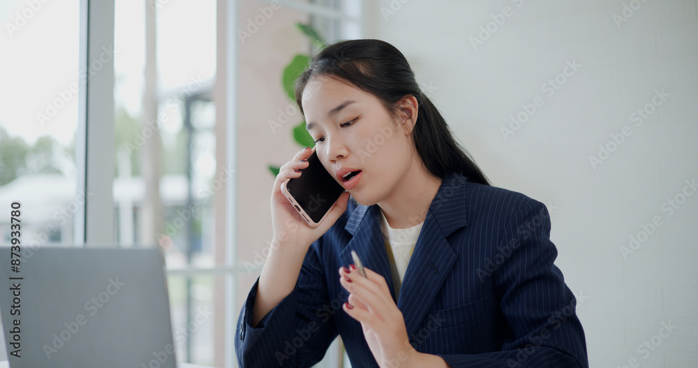 Portrait of Asian businesswoman in suit talking a cell phone while working on laptop at small coffee shop. Work from anywhere, Remote working Portrait of Asian businesswoman in suit talking a cell phone while working on laptop at small coffee shop. Work from anywhere, Remote working