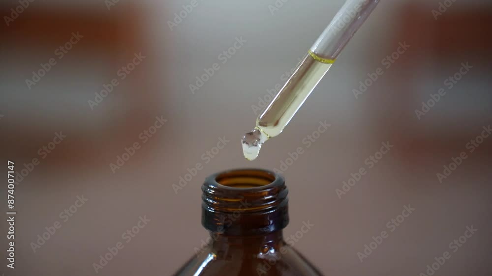 A female hand dripping from a pipette cosmetic liquid, serum above the brown glass bottle A female hand dripping from a pipette cosmetic liquid, serum above the brown glass bottle