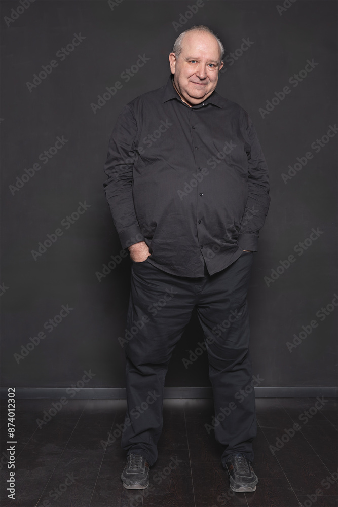 Full-length portrait of an overweight 60-year-old man posing in relaxed attitude looking at camera on gray background. Concept of aging and overweight Full-length portrait of an overweight 60-year-old man posing in relaxed attitude looking at camera on gray background. Concept of aging and overweight
