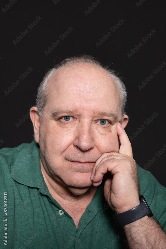 Portrait of a 60-year-old gray-haired man with blue eyes, looking at serious camera with thoughtful expression and one hand resting on his face. Black background and copy space. Concept of aging Portrait of a 60-year-old gray-haired man with blue eyes, looking at serious camera with thoughtful expression and one hand resting on his face. Black background and copy space. Concept of aging