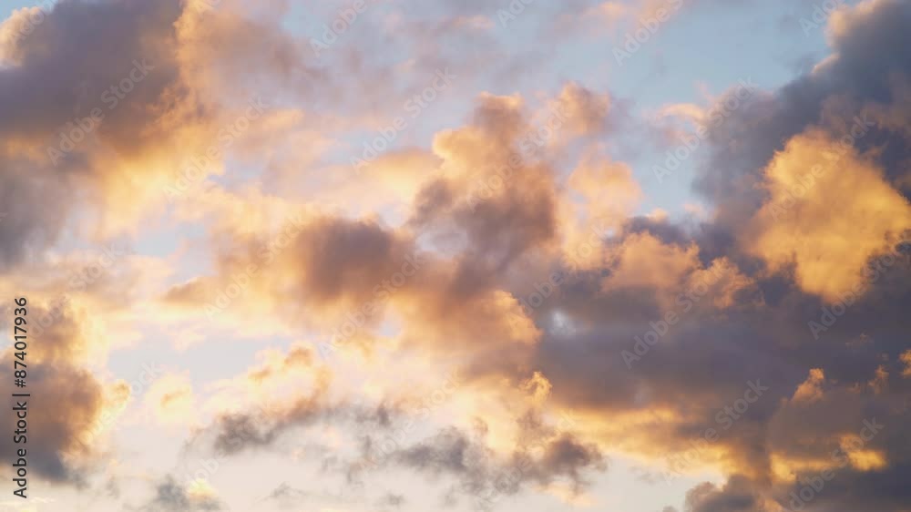Quick moving soft fluffy clouds glow pink and red against blue sky at sunset, stunning natural background on a windy day