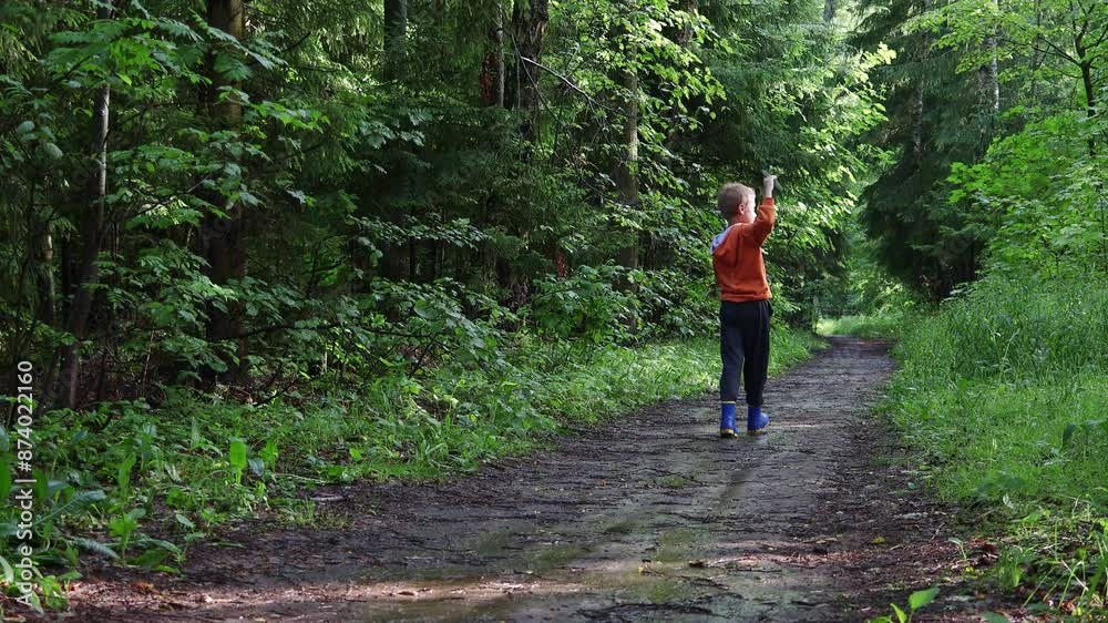 Boy in an orange hoodie and rubber boots walks in woods after rainstorm and plays airplane. Boy in an orange hoodie and rubber boots walks in woods after rainstorm and plays airplane.