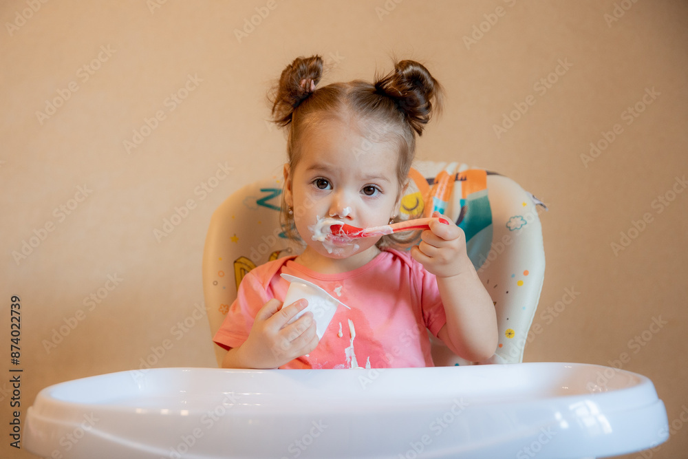 A little girl is sitting on a high chair eating at home A little girl is sitting on a high chair eating at home