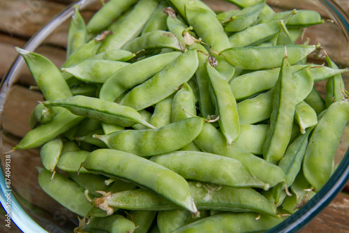 Freshly gathered pea pods in a bowl on a wooden table