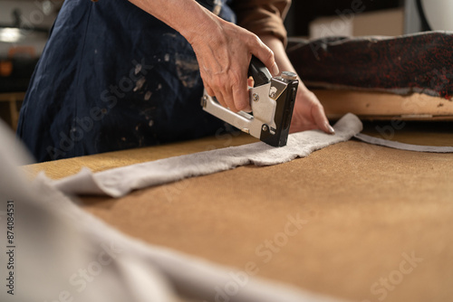 Female carpenter using pneumatic stapler after replace upholstery fabric to the Seat for armchair. furniture restoration woodworking concept