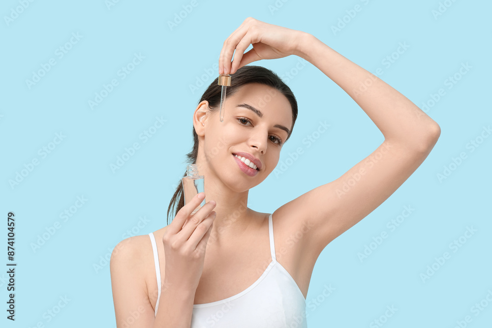 Beautiful young woman with pipette applying face serum on blue background Beautiful young woman with pipette applying face serum on blue background