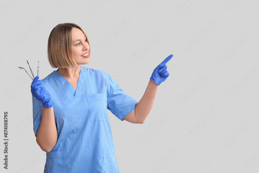 Female dentist with tools pointing at something on grey background Female dentist with tools pointing at something on grey background