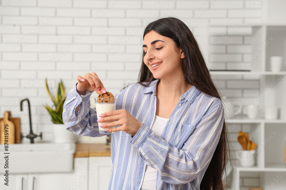 Beautiful young happy woman holding tasty cookie with chocolate chips and glass of milk at home Beautiful young happy woman holding tasty cookie with chocolate chips and glass of milk at home