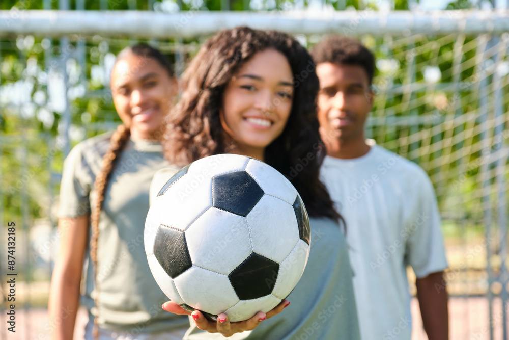 Young woman smiling and holding a soccer ball with her teammates out of focus behind her