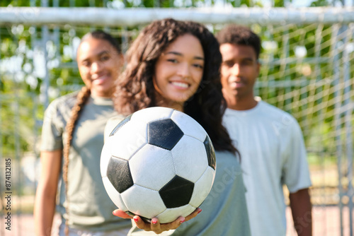 Obraz na płótnie Young woman smiling and holding a soccer ball with her teammates out of focus behind her w salonie