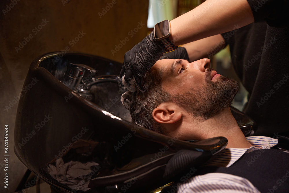 Professional hair stylist washing adult man hair using haircare agent