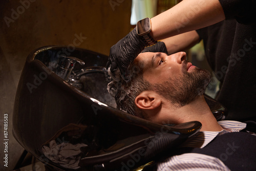 Obraz na płótnie Professional hair stylist washing adult man hair using haircare agent w salonie