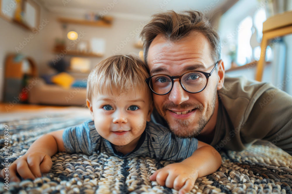 Father with glasses and beard taking a selfie with his young son on the living room floor