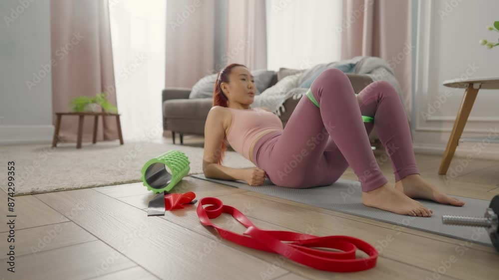 Athletic woman training with resistance band, exercises for inner thigh surface. Asian lady in sportswear practicing physical exercise for legs, lying on floor in living room, home fitness and sport