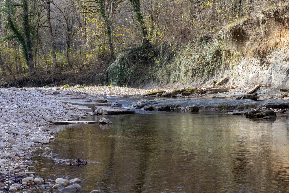 A shallow riverbed with an exposed rocky bottom, a small stream and a flow of water, autumn in nature A shallow riverbed with an exposed rocky bottom, a small stream and a flow of water, autumn in nature