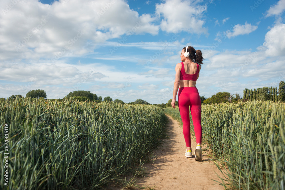 Fototapeta premium rear view of a fit sporty woman wearing red sports clothing walking through a field, 10k steps concept.