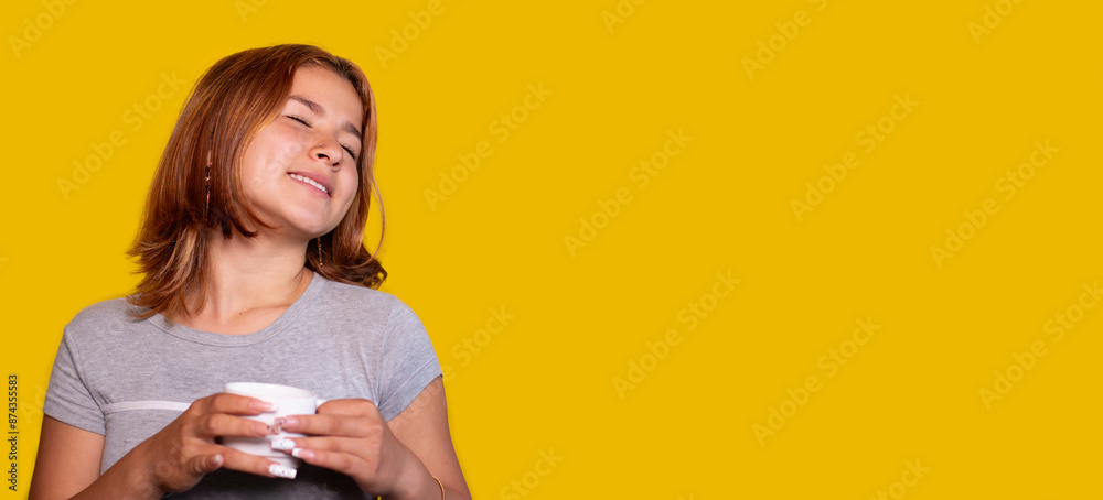 smiling teenager enjoys a hot drink in the morning. yellow background smiling teenager enjoys a hot drink in the morning. yellow background