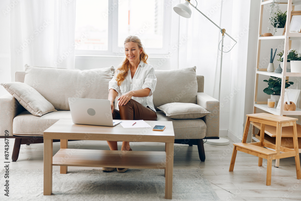 Woman working on laptop in cozy living room with bookshelf and coffee table for home office concept Woman working on laptop in cozy living room with bookshelf and coffee table for home office concept