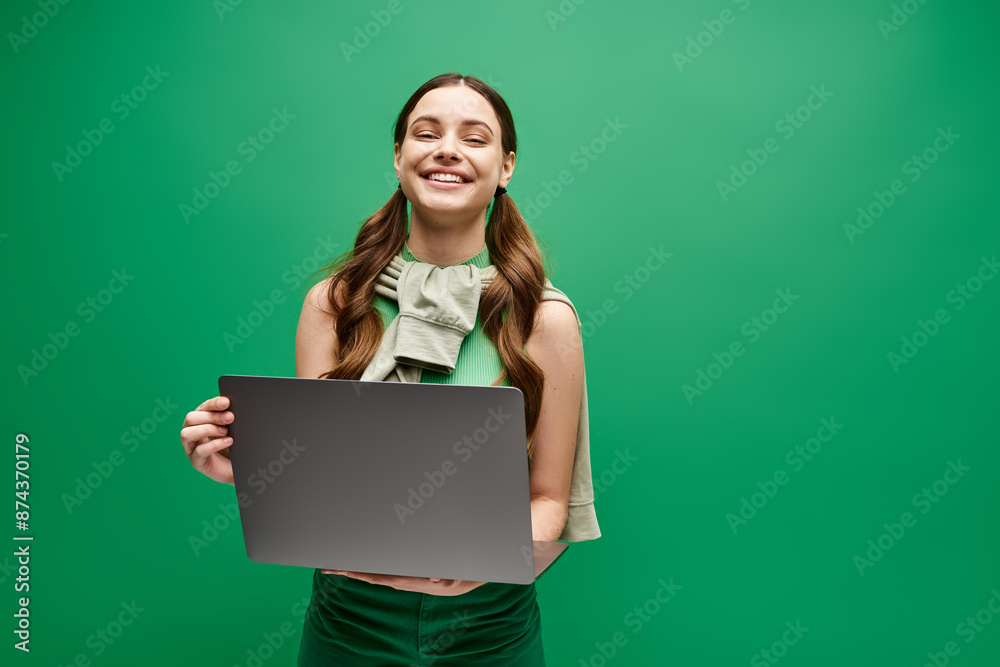 A woman in her 20s holding a laptop in front of a vibrant green background, exuding digital empowerment and connection. A woman in her 20s holding a laptop in front of a vibrant green background, exuding digital empowerment and connection.