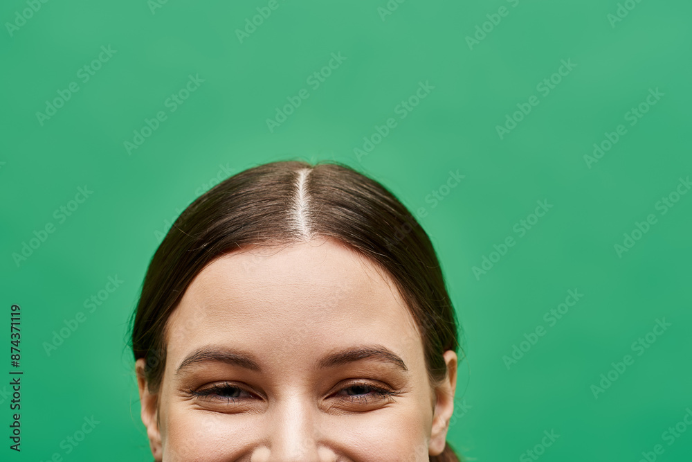 Fototapeta premium A young woman in her 20s, radiating joy with a captivating smiling eyes in a studio setting with a green background.