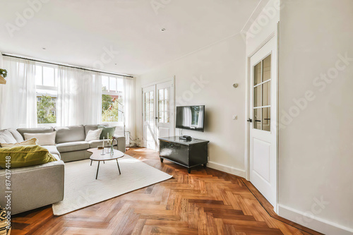 Bild auf Leinwand A bright, airy living room featuring large windows, hardwood flooring, and comfortable modern furnishings under warm daylight