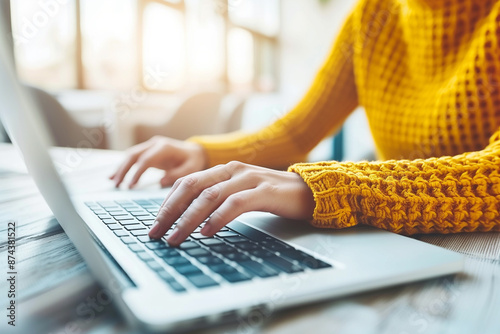 A woman is typing on a laptop in a yellow sweater photo