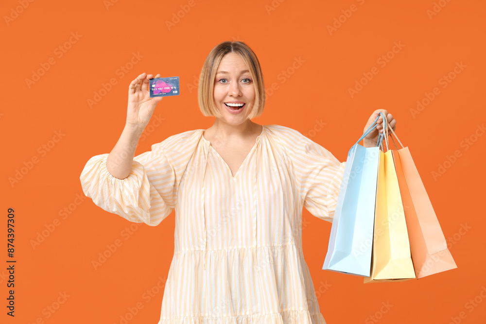 Surprised adult woman with shopping bags and credit card on orange background Surprised adult woman with shopping bags and credit card on orange background