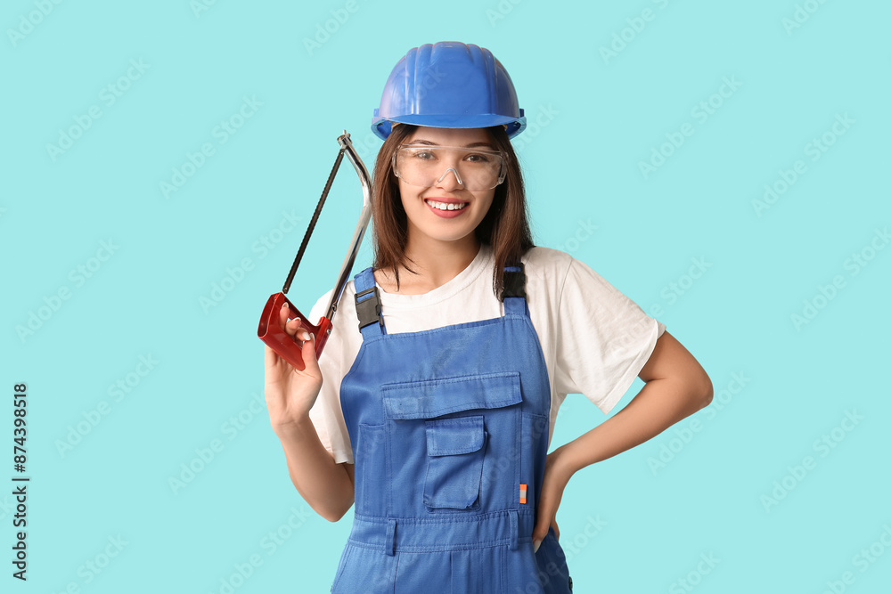 Young female worker with hacksaw on blue background Young female worker with hacksaw on blue background
