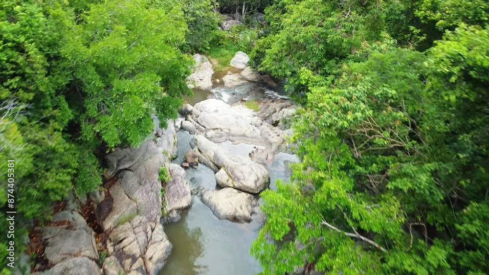 Aerial view of a serene stream flowing through a lush tropical forest, surrounded by dense greenery and rocky formations on Koh Phangan, Thailand. Aerial view of a serene stream flowing through a lush tropical forest, surrounded by dense greenery and rocky formations on Koh Phangan, Thailand.
